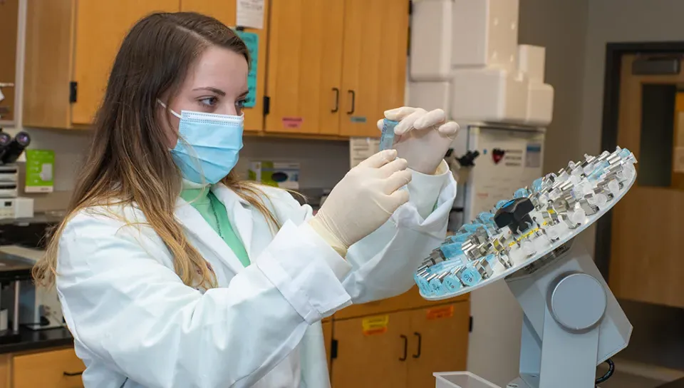 A student in a white lab coat and mask reviewing slides